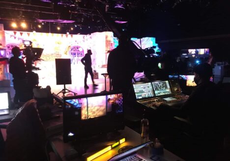 A film crew behind a lighting console on set in a television studio.